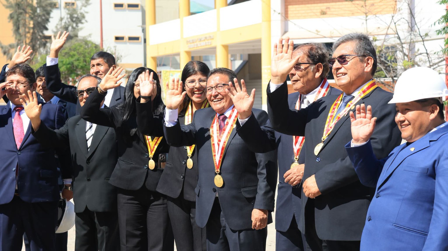 Participantes de una ceremonia universitaria saludando juntos